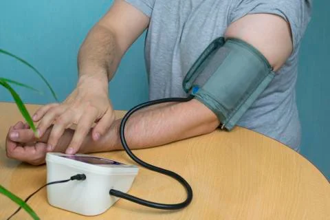 A man changes his pressure by a tonometer sitting at a table with a cuff on h Stock Photos