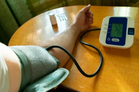 A man changes his pressure by a tonometer sitting at a table with a cuff on h Stock Photos