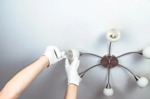 A man changes a light bulb in a chandelier at home Stock Photos