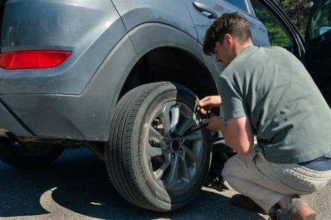 Man changes tire on gray crossover car on sunny day on the side of the road. Stock Photos