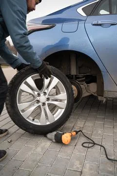 A man changes the wheel on a blue car with a wrench Stock Photos