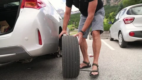 Man changing a flat tire on a white car in a parking lot during daytime roadside Stock Footage 318259221