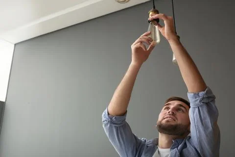 Man changing lamp light bulb indoors. Space for text Stock Photos