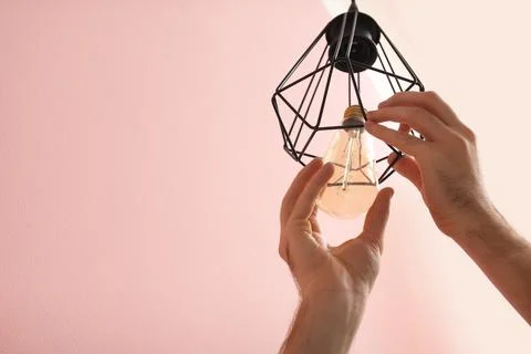 Man changing light bulb in lamp on color background. Space for text Stock Photos