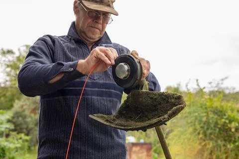 Man changing orange trimmer line on string trimmer head. Gardener reparing 写真素材