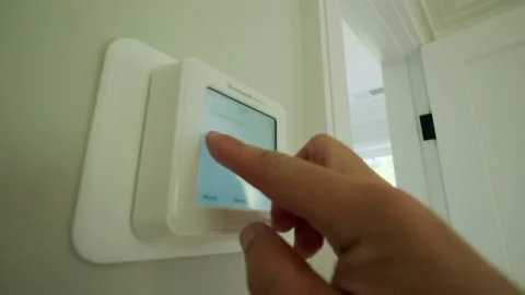 Man changing the temperature on a programmable hvac system on the house wall Stock Footage 205172572