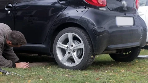 Man changing tires, jacking up car and loosening lugnuts Stock Footage 97402937