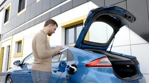 Man is charging an electric car while standing at a station,holding tablet Stock Footage 282885835