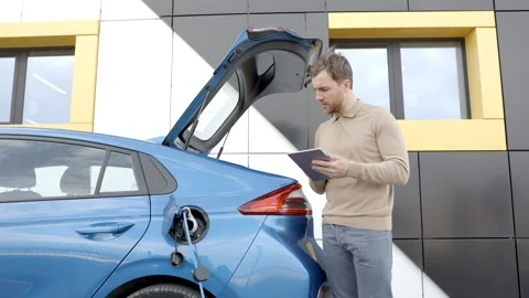Man is charging an electric car while standing at a station,holding tablet Stock Footage 282885837