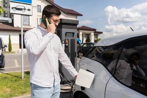 Man Charging Electric Car While Talking on Mobile Phone Stock Photos