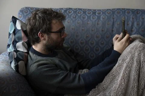 A man chats with his smartphone while he rests on the sofa Stock Photos