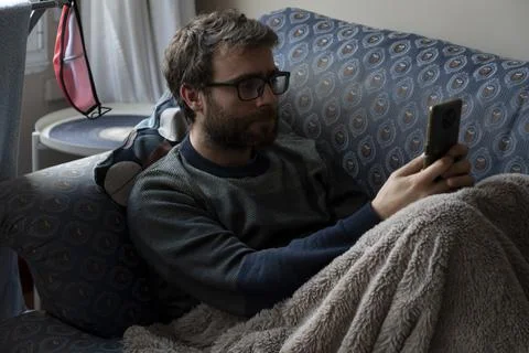A man chats with his smartphone while he rests on the sofa Stock Photos