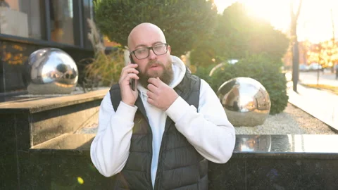 Man chatting on phone outside building during sunset surrounded by modern decor Stock Footage 346726071
