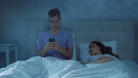 Man Chatting on Phone While Girl is Sleeping at Night. Man Using Phone in Bed Stock Footage 217425504
