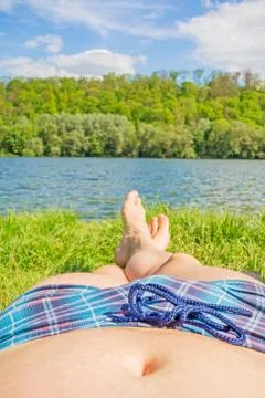 Man with checkered bathing slip and bare feet at lake / river, meadow / grass Stock Photos