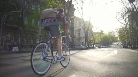 Man in a checkered shirt with a backpack riding his bike slow motion Stock Footage 76132035