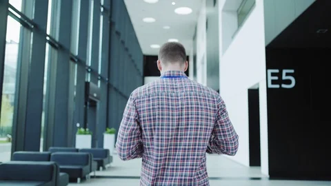 Man in checkered shirt walking down office lobby Stock Footage 112052535