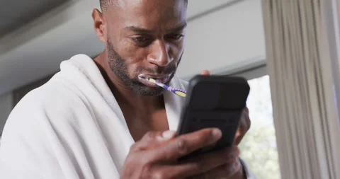 Man is checking black phone and brushing teeth with purple-yellow brush near Stock Footage 341852240