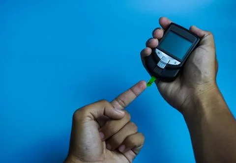 Man checking blood sugar level using glucometer. Diabetes concept on blue bac Stock Photos