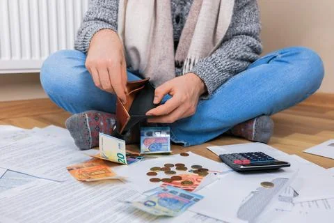 Man checking empty wallet sitting on floor near radiator with bills and mon.. Stock Photos