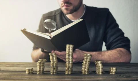 Man Checking Finances using magnifying glass with coins on stacks Foto stock