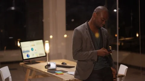 Man checking his mobile phone and smiling at camera at night in office Stock Footage 107628768