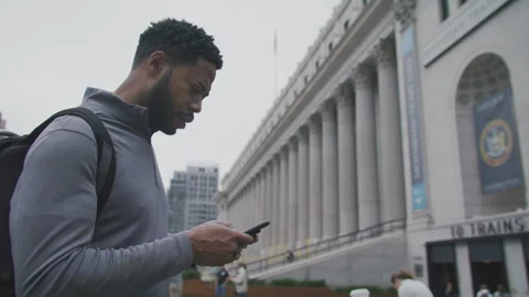 Man checking his phone outside a historic building on a cloudy day Stock Footage 312591430