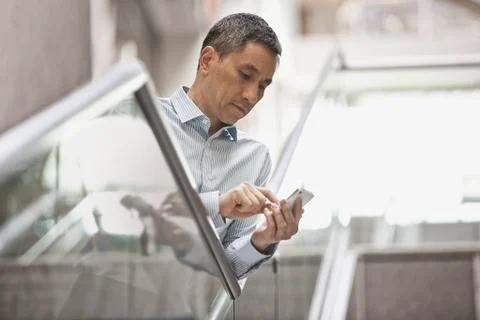 A man checking his smart phone in a large airy building with windows. Fotos de archivo