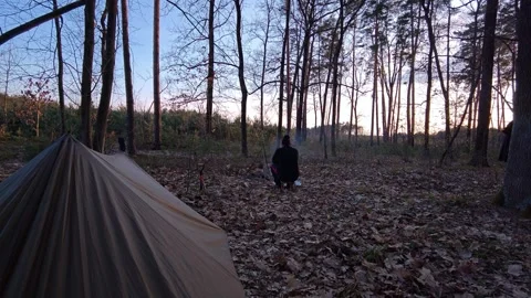 Man checking his tarp shelter in a wild forest at sunset Stock Footage 333844814