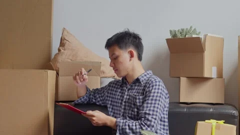 Man checking off items on moving inventory list with cardboard boxes sits on Stock Footage 336287743