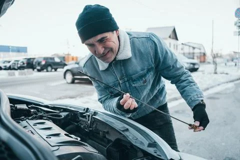 Man checking low or dirty engine oil in a car during winter, noticing problem Stock Photos