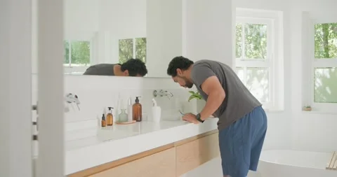 Man checking mirror turning tap rinsing mouth placing toothbrush in holder at Stock Footage 341394301
