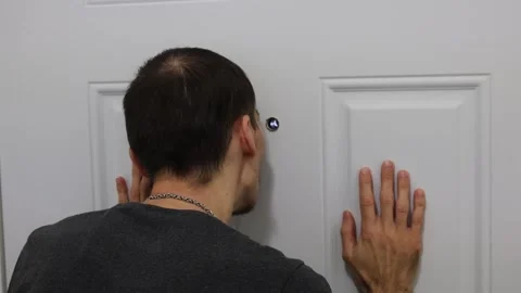 Man checking peephole with hands on door home security fear concept Stock Footage 331769582
