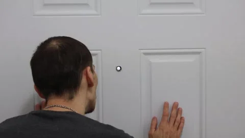Man checking peephole with hands on door home security fear concept Stock Footage 331769583