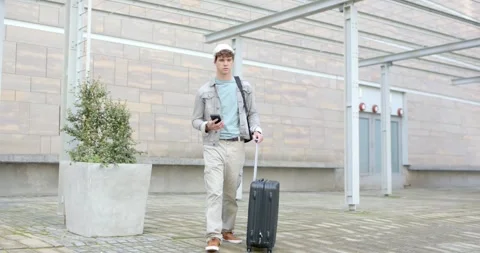 Man checking phone for directions walking through paved plaza pulling suitcase Stock Footage 317638188