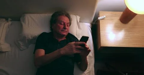 Man checking phone at night in bed, top view. Old Senior person using smart.. Stock Photos