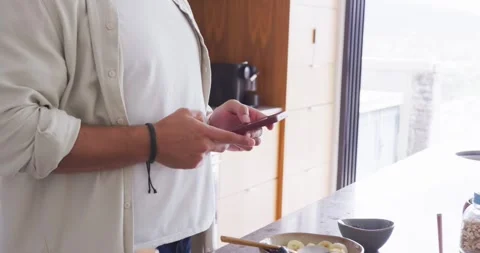 Man checking phone, stirring bowl with spoon, putting on headphones for 스톡 동영상 344318663