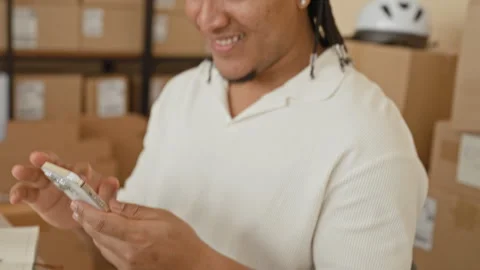 Man checking smartphone and smiling while preparing parcels in a building; .. Stockbeeldmateriaal 339165043