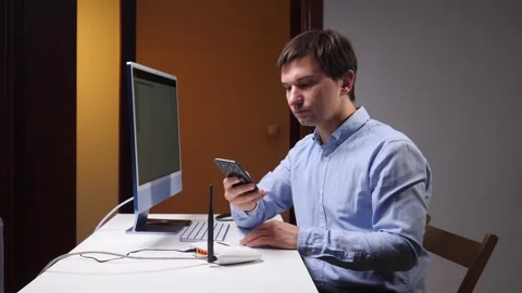 Man checking a smartphone at a computer workstation, using a wireless router Stock Footage 348113690