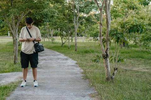 Man checking smartphone in a park with shoulder bag Stock-Fotos