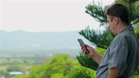 Man checking smartphone while standing on balcony with scenic mountain Stock Footage 277618007