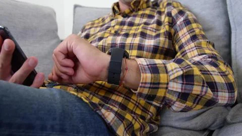 Man is checking smartwatch and using smartphone on couch cushions in flat design Foto stock