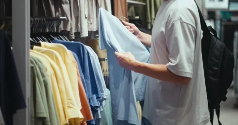 Man checking t-shirts in store, store boosting variety of casual apparel, store Stock Footage 312122631