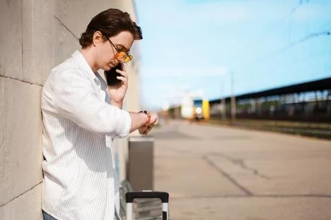 Man checking time on his watch and talking on a smartphone while waiting on.. 스톡 사진
