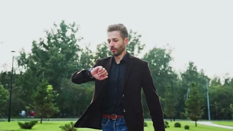 Man checking watch while walking through a city park in the afternoon Stock-Footage 294042154