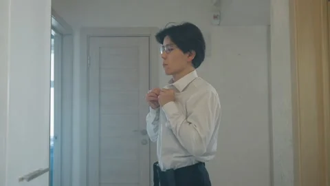 Man checks appearance. Confident man adjusts tie in mirror before leaving. Asian Stock Footage 337230960