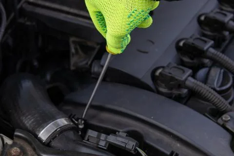 Man Checks Engine Oil Level With a Dipstick While Wearing a Green Glove Und.. Stock Photos