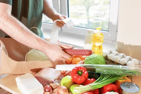 A man checks a grocery receipt while unpacking fresh food from a paper bag,.. Foto stock