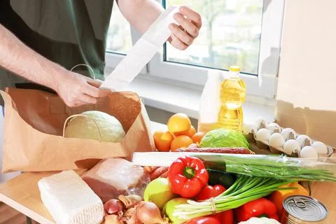 Man checks a grocery receipt while unpacking fresh food from a paper bag, i.. Stock Photos