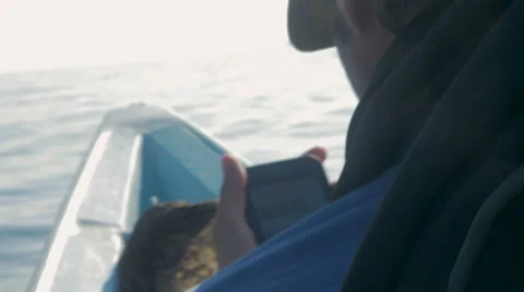 A man checks his phone while sitting at the front of a small boat Stock Footage 57103693